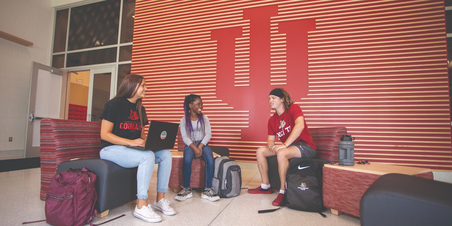 Three students sitting in front of the IU trident.